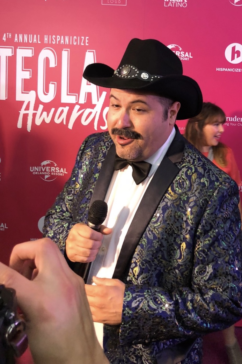 Tiburcio on the red carpet at the Tecla Awards holding a microphone.